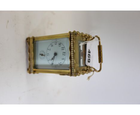 A SMALL EARLY 20TH CENTURY BRASS CARRIAGE CLOCK, serpentine edged case with white enamel dial and alarm, on turned feet, 4 in