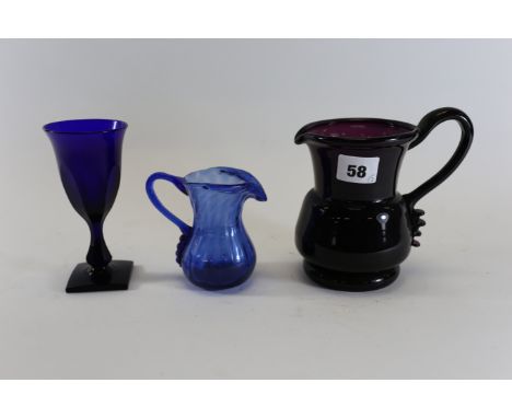 A 19TH CENTURY AMETHYST GLASS JUG with crimped end handle, 5 ins high, a ditto smaller blue JUG, 3 1/2 ins high and a British