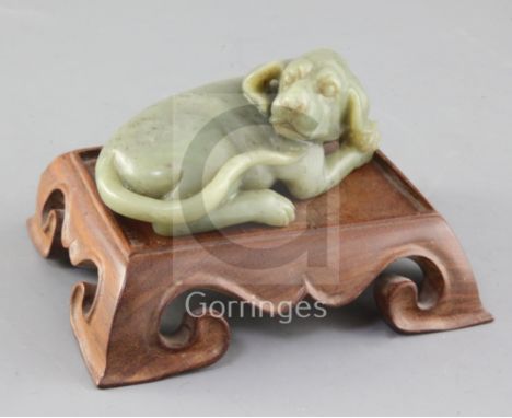 A Chinese green jade figure of a recumbent dog, the stone with slight brown inclusions, length 12.5cm excl. wood stand