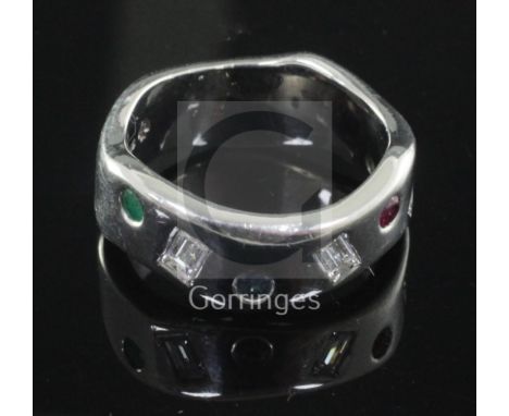 A modernist wavy design 18ct white gold, emerald, ruby, sapphire and baguette cut diamond gypsy set ring, size R.