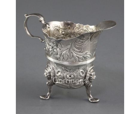 A mid 18th century Irish silver tripod milk jug, by William Townsend? with repousse floral decoration and engraved armorial, 