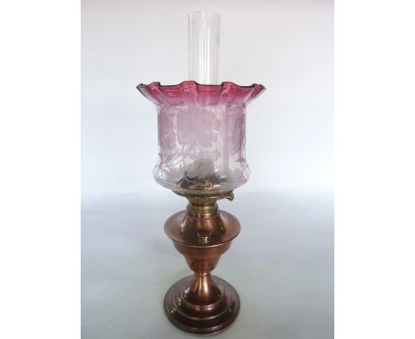 An oil burning lamp with copper fount accommodating a brass burner stamped Augusta-Brenne supporting a good quality cranberry
