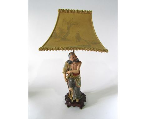 An unusual early 20th century ceramic table lamp in the form of a Japanese style male character in ochre and green coloured r