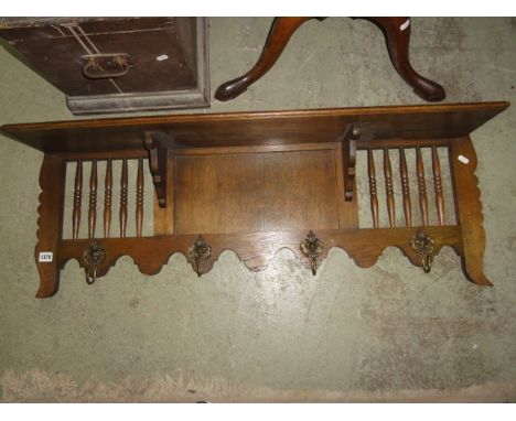 An oak wall mounted coat rack with simple shelf supported by shaped brackets flanked by turned spindle panels over four decor