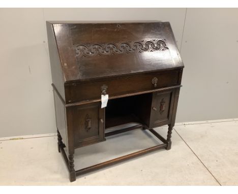 A dark oak Tudor style bureau with a decorative carved front, single drawer above cupboard doors, width 91cm, depth 42cm, hei