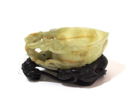 A Chinese Jade Libation Cup, in the form of a peach with pierced foliate scroll handle, 12cm long, on hardwood base See illus