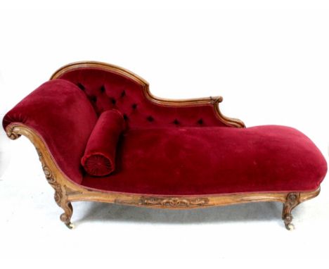 A Victorian walnut-framed chaise longue upholstered in red button-back velour, with carved scroll and on squat cabriole legs,
