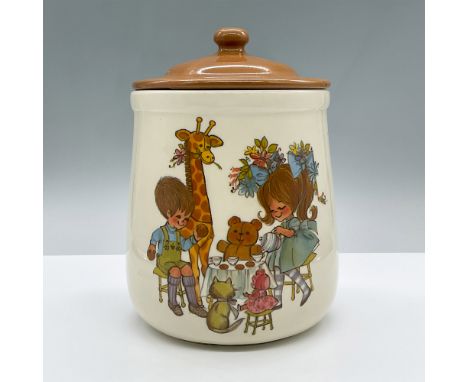 A quaint white cookie jar with an image of a boy and girl having a tea party along with a giraffe, a doll, a teddy bear, and 