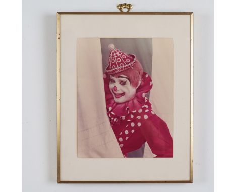 A vibrant photograph of a clown, dressed in a whimsical costume with a polka-dot ruffled collar and beaded party hat, peeking