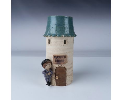 This whimsical Märchen House ceramic vase stands at 8"H and features a playful design of a child leaning against the door of 
