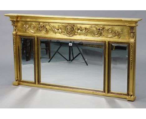 A reproduction gilt-frame triple panel overmantel mirror with neo-classical style relief decoration to the frieze of scrolls,