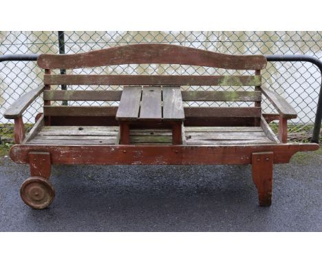 A teak slatted garden bench/table with wheels to the left-hand side, 63½” long.