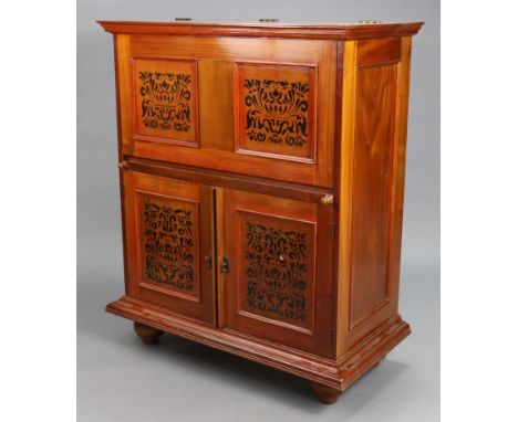 An eastern hardwood drinks cabinet enclosed by a hinged lift-lid &amp; fall-front above a cupboard enclosed by pair panel doo