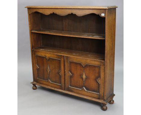 An early 20th century Jacobean-style oak bookcase, fitted with an open shelf above a cupboard enclosed by pair of panel doors