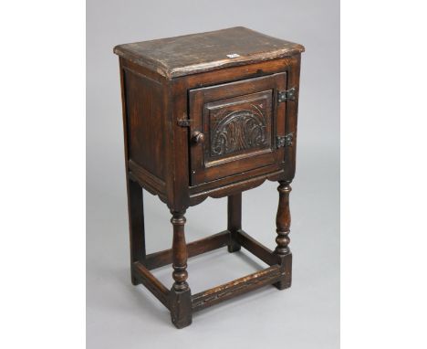 A reproduction oak bedside cupboard enclosed by carved panel door, on baluster-turned legs with plain stretchers, 17¾” wide x