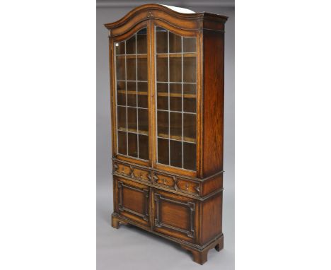 An early 20th century Jacobean-style oak tall bookcase with shaped top, having three adjustable shelves enclosed by pair of l