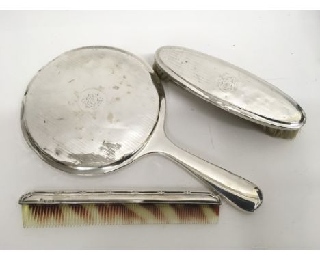 A three piece silver backed dressing table set comprising a hand mirror, brush and comb, hallmark for Birmingham William Neal