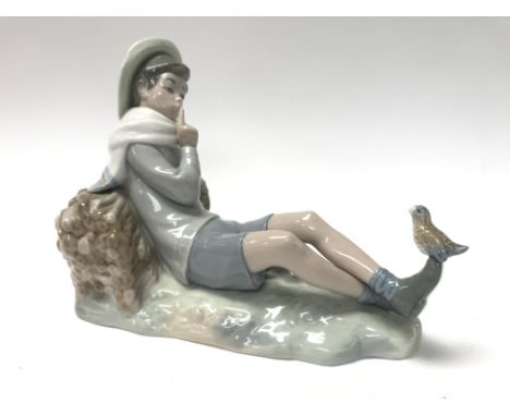 A Lladro figure of a reclining boy with a songbird perched on his shoe.