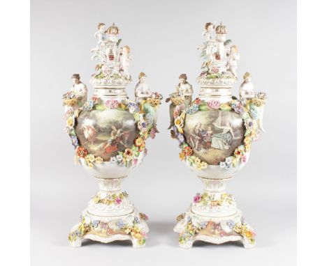 A LARGE PAIR OF DRESDEN STYLE TWO HANDLED URNS, COVERS AND STANDS, the lids with crest and two cupids, the vase painted and e