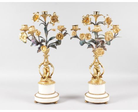 A GOOD PAIR OF LOUIS XVI PATTERN ORMOLU AND WHITE MARBLE FOUR LIGHT CANDELABRA, formed as cupids sitting beneath scrolling br