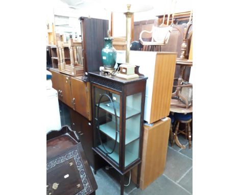 A narrow display cabinet with carved wood detail, a brass lamp, a ceramic and brass lamp base and a small glass paneled corne