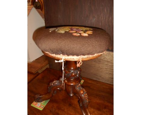 A 19th C walnut revolving piano stool the tapestry upholstered seat raised on floral carved supports and three out swept legs
