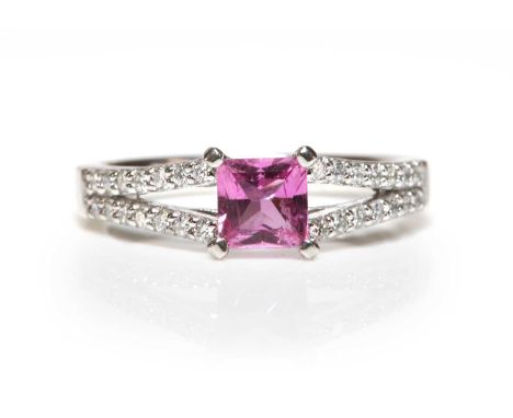 A platinum single stone pink sapphire ring,with diamond set shoulders. A princess cut pink sapphire, four claw set at the cor