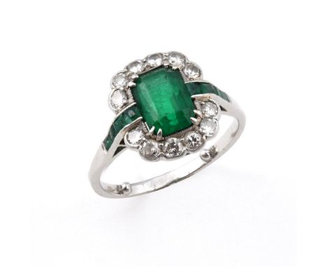 AN EMERALD &amp; DIAMOND RING. the rectangular-shaped emerald is set within a surround of twelve circular old-cut diamonds, w