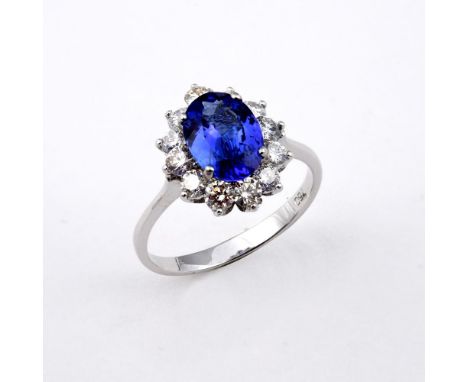 A TANZANITE AND DIAMOND CLUSTER RING. the oval-shaped tanzanite weighs 1.71 carats and is set within a surround of twelve rou