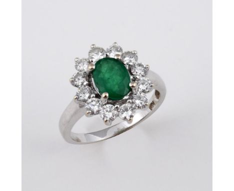 AN EMERALD AND DIAMOND CLUSTER RING. the oval-shaped emerald is set within a surround of twelve brilliant-cut diamonds, in 18