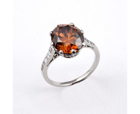 A FANCY COLOURED DIAMOND SOLITAIRE RING. the round cut fancy brown diamond is set with six square-cut diamonds to each should