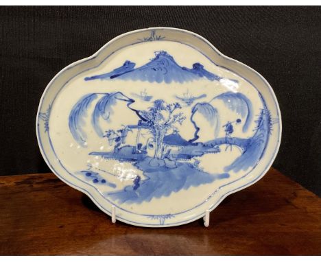 A Chinese quatrefoil lobed shallow dish or tray, of silver shape, painted in tones of underglaze blue with a figure in a monu