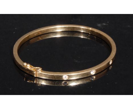 A diamond set hinged bangle, stamped '750' for 18ct gold, quite plain, set with five brilliant cut stones, 6cm interior diame