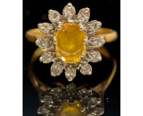 A diamond, yellow sapphire and 18ct gold cluster ring, central oval raised claw set stone within twelve circular brilliant cu