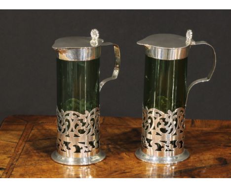 A pair of Edwardian silver mounted green glass liqueur jugs, hinged covers with anthemion thumb pieces,  pierced scroll bases