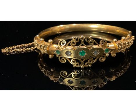 A Victorian 9ct gold diamond and emerald hinged bangle, the two old brilliant cut diamonds centered and flanked by facet cut 