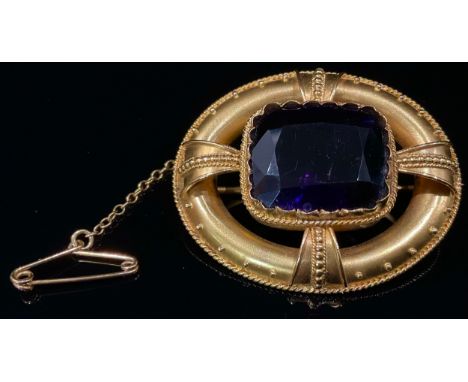 A Victorian amethyst and gold coloured metal oval brooch in the Etruscan revival manor, the central rectangular facet cut sto