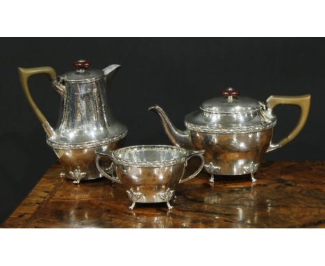 An Arts and Crafts silver three piece tea service, comprising teapot, hot water pot and sugar basin, planished overall, hinge