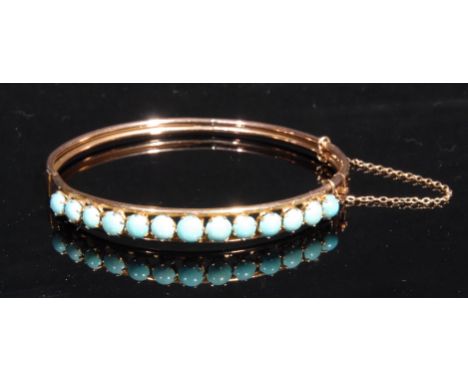 A gold coloured metal hinged bangle, claw-set with a row of turquoise cabochons, 6cm diam, 9.7g gross 