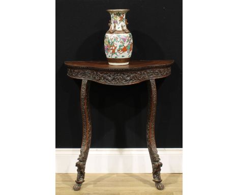 A 19th century Burmese hardwood serpentine console table, slightly oversailing top above a deep frieze carved with a figure, 