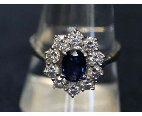 An 18ct white gold sapphire and diamond cluster ring, the oval sapphire surrounded by ten diamonds. Estimated total diamond w