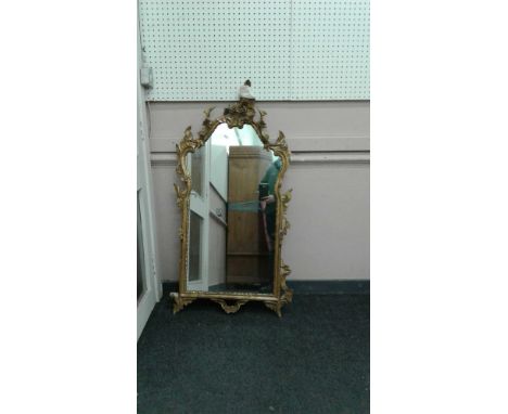 in the Rococo taste, the foliate gilt frame enclosing a shaped mirror panel, 62 cm wide