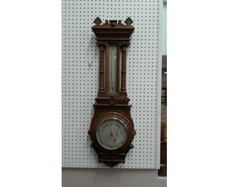 the carved pediment resting on a dual scale thermometer flanked by carved turned pillars above a circular aneroid barometer, 