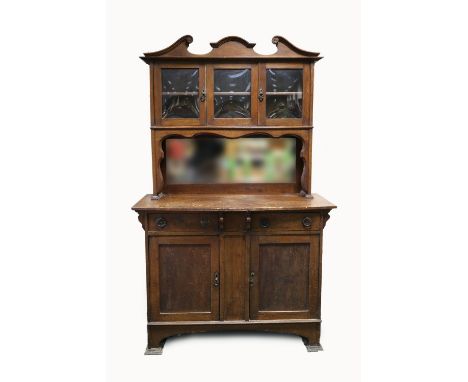 An Edwardian oak mirror back side board in Liberty's style with scrolling swan neck pediment above a glazed panel flanked by 