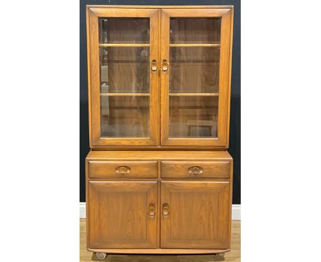 An Ercol bookcase, the upper section with glazed doors enclosing two shelves, the projecting base with a pair of frieze drawe