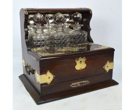 An Edwardian oak tantalus/compendium with plated mounts, the raised back section set with three square section hobnail cut de