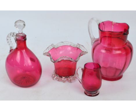 Four pieces of Victorian cranberry tinted glass comprising a large jug, small footed jug, shaped bowl and decanter with cut g