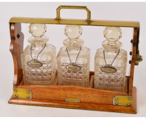 An Edwardian oak and silver plate mounted three bottle tantalus, each square section decanter set with contemporary hallmarke