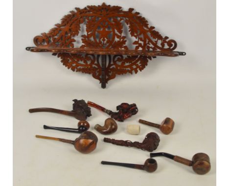 An early 20th century fret cut wall mounted pipe rack decorated with oak leaves and acorns, and a small quantity of pipes inc