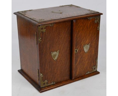 A 1920s oak smoker's cabinet with electroplated mounted corners and two shields on the pair of doors enclosing two small draw